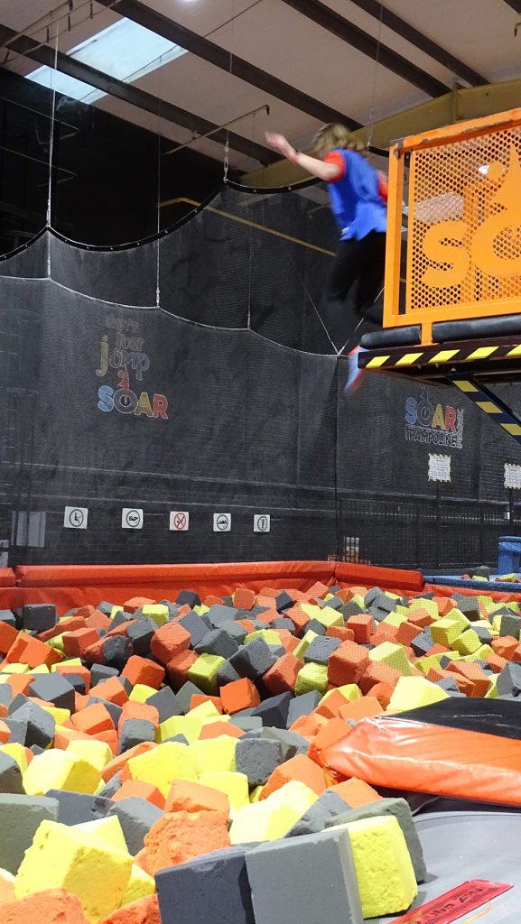 A Guide jumps from a high platform into foam cubes at Soar trampoline park.